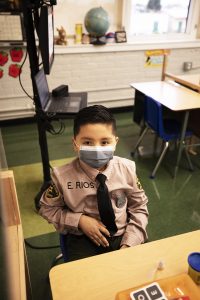 A Resurrection School student dressed as a police officer sits at his desk, spaced out from his classmates and surrounded by Plexiglass, ready for in-person learning. (Victor Alemán)