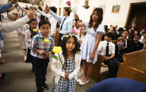 (Right to left): Seventh-grader  Clarissa Del Rosario stands with a flower while first-graders Melina Hernandez, Roman Munoz and Eliza Espiritu walk under the arch of flowers during a May 5 May Crowning Mass at St. Dorothy in Glendora. (Victor Alemán)