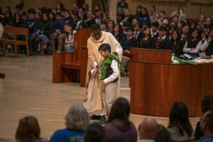 Father Frederick Byaruhanga, a priest originally from the Diocese of Kabale in Uganda and now a chaplain for the VA Greater Los Angeles, has a student help him during his homily for the annual Missionary Childhood Association Youth Appreciation Mass on Oct. 16. (John Rueda) 