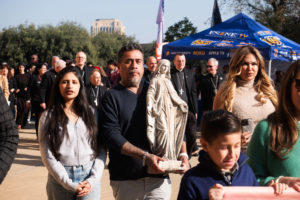 George Magallon processes into the OneLife LA celebration on Jan. 18 holding the Virgin Mary statue that survived the Eaton Fire at his home. With him are his wife, Jennifer, and daughter, Sophia. (Victor Alemán)