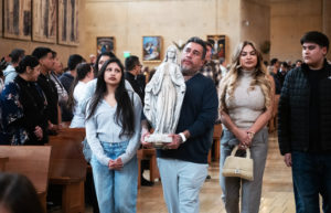 George Magallon processes into the OneLife LA celebration on Jan. 18 holding the Virgin Mary statue that survived the Eaton Fire at his home. With him are his wife, Jennifer, and children, Sophia and Diego. (Victor Alemán)