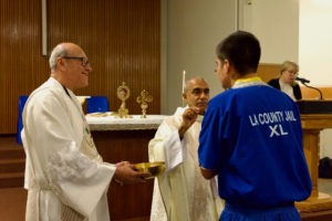 Msgr. Anthony Figueiredo offers Communion to an inmate during a Mass in honor of St. Carlo Acutis' relic visit to LA Men’s Central Jail on Oct. 20. (Reese Cuevas)