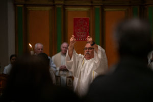 Deacon José Luis Díaz, who helped save Sacred Heart Church in Altadena from burning in 2025, holds up the book of Gospels during a Jan. 7 healing Mass on the one-year anniversary of the Eaton Fire. (John Rueda)