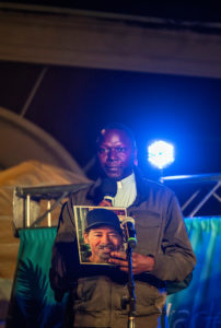 Father John Kyebasuuta, pastor of St. Elizabeth of Hungary Catholic Church in Altadena, holds a picture of Eaton Fire victim Victor Shaw at a Jan. 7 interfaith vigil marking one year since the fire.  (Juanito Holandez Jr.)