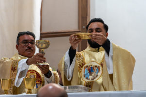 Father David Zamora holds the Eucharist along with his father, Miguel, a deacon, during his first Mass at his home parish of Sacred Heart Church in Lancaster on May 31. (Katie Trejo)